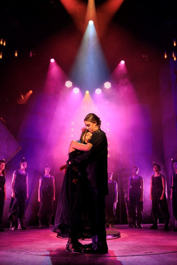 Performers embrace under purple wash lighting