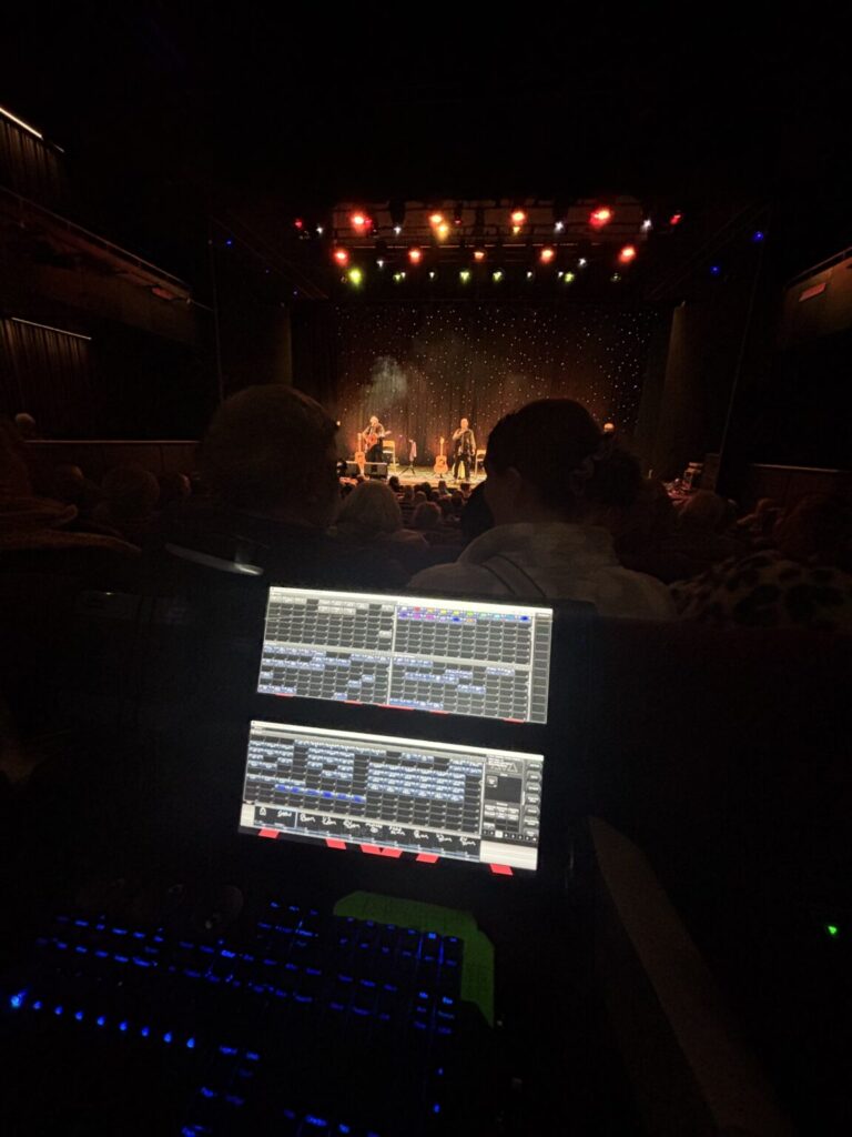 Pontio Arts at Bangor University: the stage is seen from the lighting desk with a full house watching a band perform.